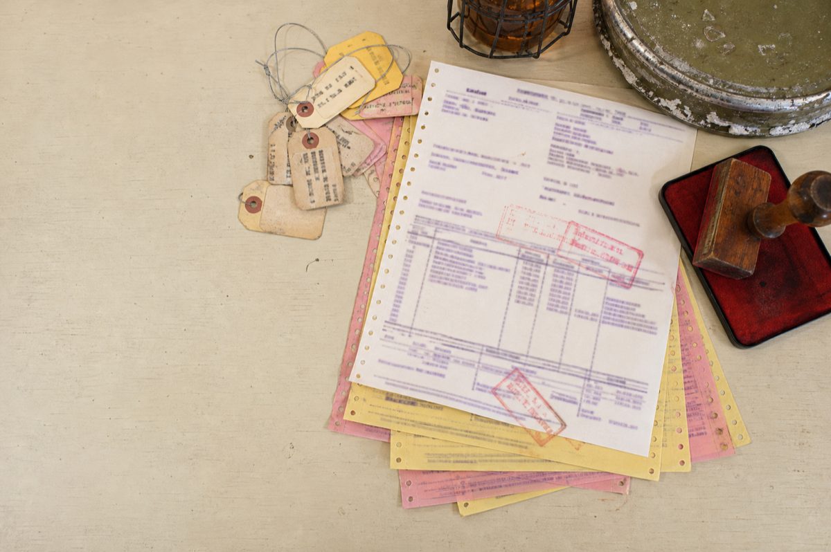 A multi-ply carbon docket, white over canary over rose, under two red customs stamps, beside a stamp block and a bundle of luggage tags.